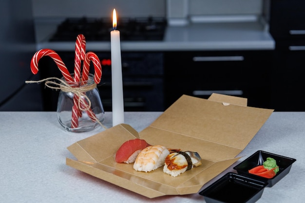 Sushi con camarones de atún y anguila se encuentra en una caja de cartón sobre la mesa en la cocina Concepto de Navidad Decoraciones festivas en forma de velas, figuritas y dulces