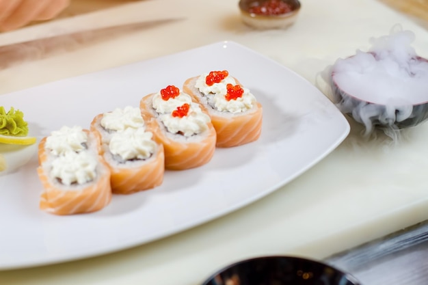 Sushi con caviar en plato. Tabla de cocina con plato de sushi. Rollos de Uramaki y hielo seco. Café de sushi durante el día.