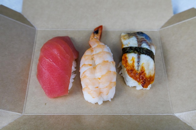 Sushi com camarão atum e enguia está em uma caixa de papelão sobre a mesa na cozinha Conceito de fast food