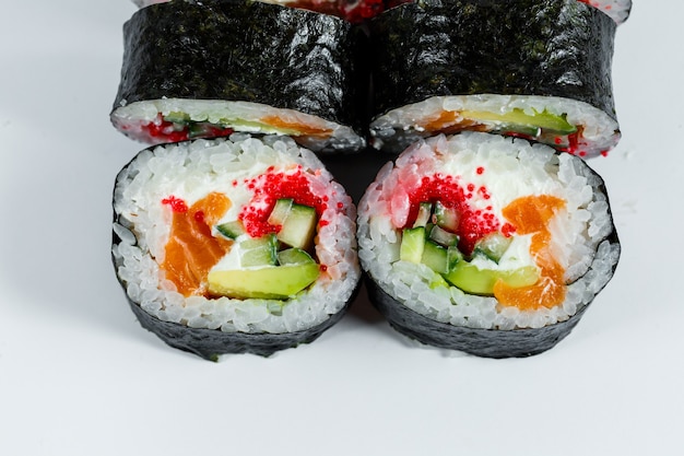 Sushi de comida japonesa en hoja de nori con aguacate, pescado fresco y caviar rojo en un plato blanco