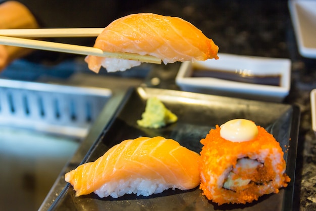 Sushi de salmão com pauzinhos e sushi japonês fresco rola sobre fundo preto