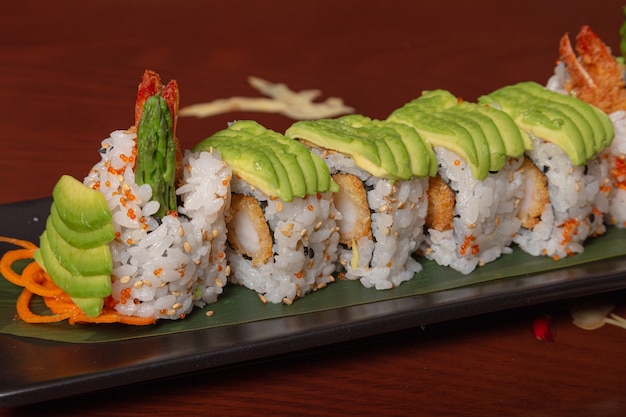 Sushi de salmão grelhado embrulhado com abacate, tempura de camarão e queijo na mesa de madeira. imagem isolada