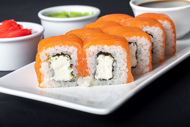 Sushi define Uramaki, Califórnia, Filadélfia, em um prato branco. Gengibre e wasabi próximos.