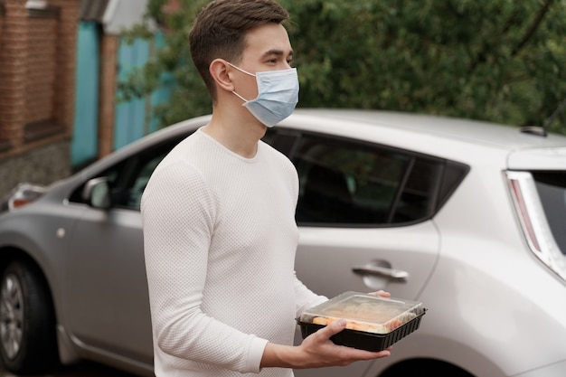 Sushi definido no serviço on-line de entrega de comida saudável de caixa de carro. Correio de homem bonito com máscara médica dá uma caixa de sushi para você. Culinária japonesa.