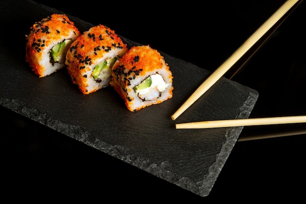 Sushi e pauzinhos tradicionais. Filadélfia com salmão, abacate e queijo. Cozinha japonesa em fundo preto.