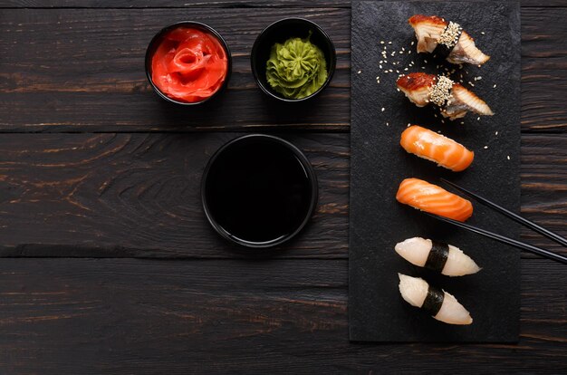 Sushi essen. Japanisches Restaurant, Unagi und Lachssushi auf dunklem Hintergrund. Stück mit Stäbchen nehmen. Draufsicht auf schwarzes Holz