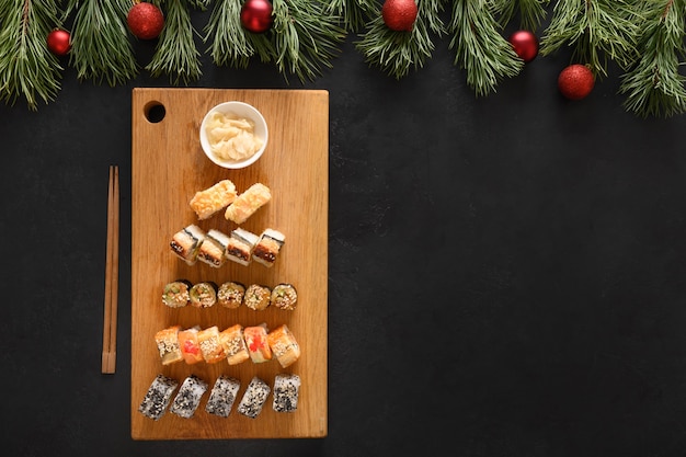 Sushi gesetzt als Weihnachtsbaum diente auf Holz Schneidebrett als Weihnachtsdekoration auf schwarzem Hintergrund. Von oben betrachten. Platz für Text. Flacher Laienstil.