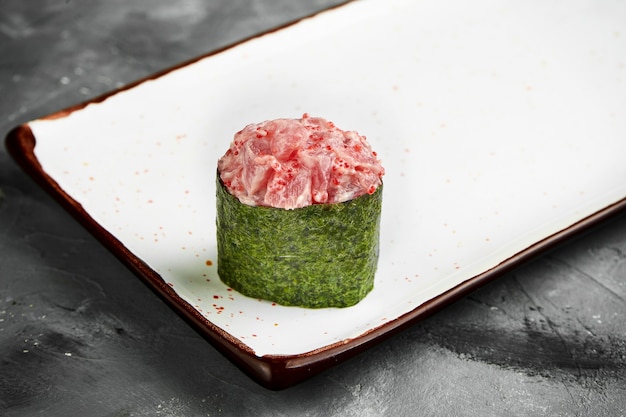 Sushi gunkan japonés tradicional con atún, caviar y salsa picante en nori en un plato blanco. De cerca, enfoque selectivo