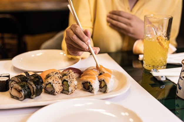 Sushi japanisches Essen Nahaufnahme mit Frauenhand in einem Restaurant Lifestyle Sashimi leckere Meeresfrüchte und Reisrollen Gelbe Farbe des Jahres