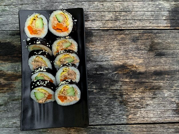sushi japonés en plato negro en mesa de madera plana makí y rollos con atún algas marinas aguacate
