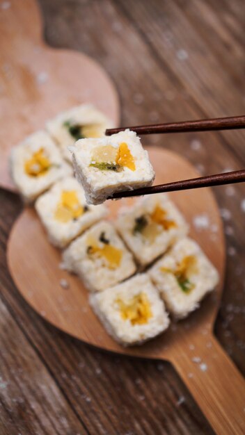 Sushi-Lieferung. Süße Brötchen aus Reis, Ananas, Kiwi und Mango. Rollen auf einem hölzernen Hintergrund. Holzstäbchen für Sushi.