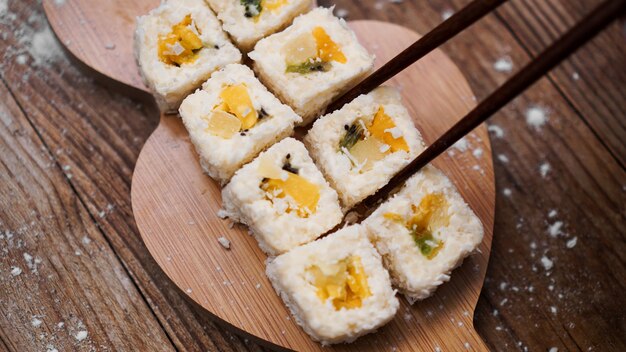 Sushi Lieferung. Süße Brötchen aus Reis, Ananas, Kiwi und Mango. Rollen auf einem Holztisch. Holzstäbchen für Sushi.