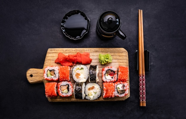 Sushi maki definido servido em um tablet de madeira com pauzinho e molho de soja na mesa preta lindos japoneses ...