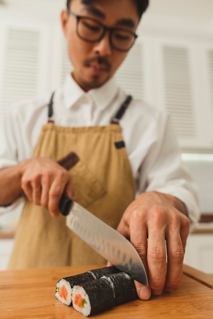 Foto sushi-meister macht sushi-rollen-porträt eines asiatischen kochs in uniform, der fertige brötchen in scheiben schneidet