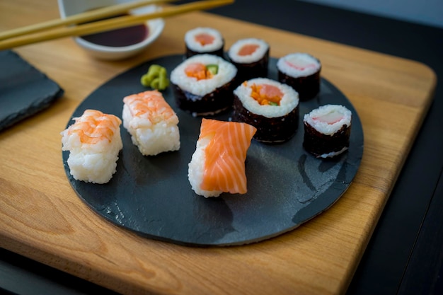 Sushi en una mesa de madera sobre un plato de pizarra negra con salsa de soja y palillos