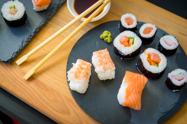 Sushi en una mesa de madera sobre un plato de pizarra negra con salsa de soja y palillos