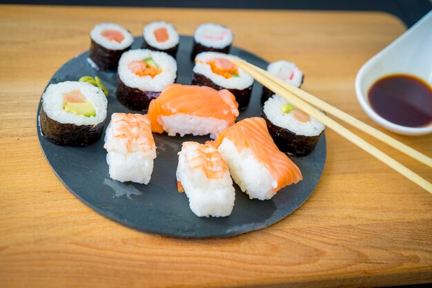 Sushi en una mesa de madera sobre un plato de pizarra negra con salsa de soja y palillos