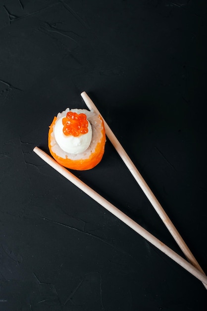 Foto sushi mit stäbchen auf schwarzem hintergrund
