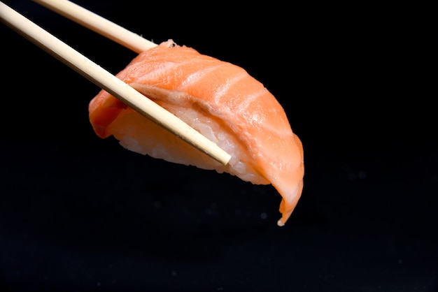 Foto sushi nigiri de salmón en palillos sobre negro