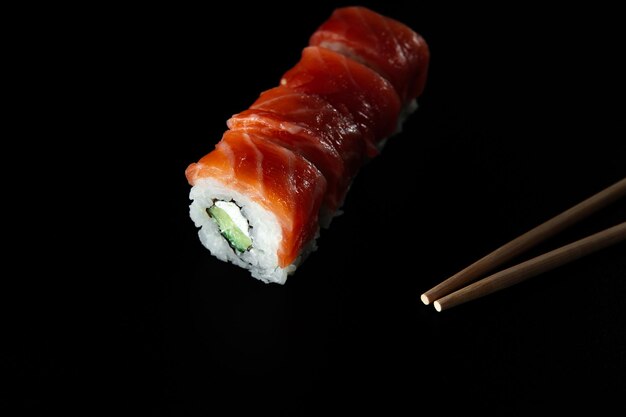 Sushi con pescado rojo sobre un fondo negro con palos de bambú