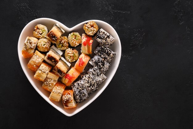 Sushi en plato como corazón sobre fondo negro. Concepto de amor de comida de San Valentín