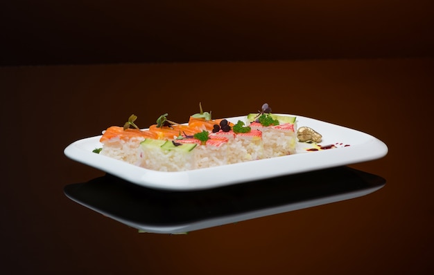 Sushi en un plato sobre un fondo marrón con reflejo. rollo de pescado