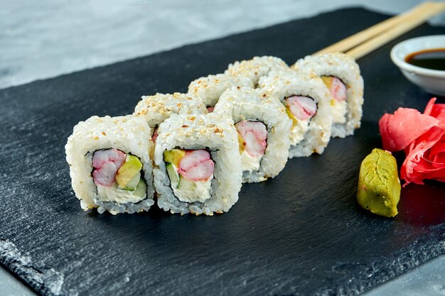 Sushi roll california em gergelim com abacate, camarão e queijo da Filadélfia em uma placa de ardósia preta.