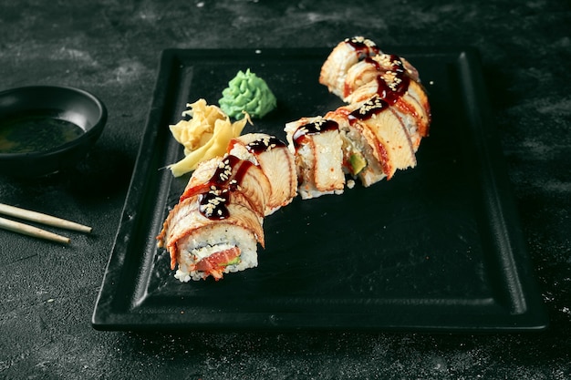 Sushi roll goldener Drache mit Aal und Lachs auf einem schwarzen Teller auf dunklem Hintergrund. Lebensmittellieferservice. japanische Küche