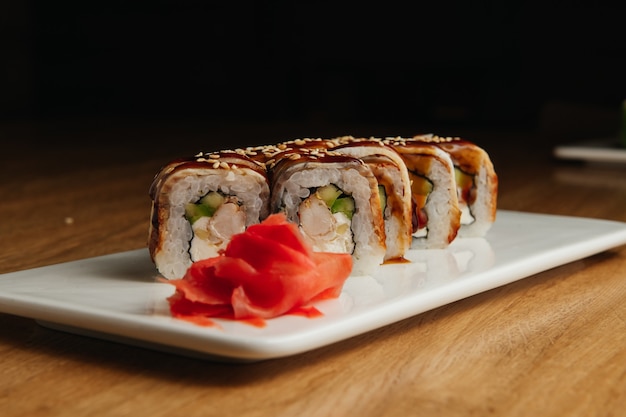 Sushi roll (Maguro) con camarones, anguila ahumada, aguacate, queso philadelphia en un plato blanco. Menú de sushi. Comida japonesa.