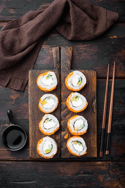 Sushi-Rolle Geisha mit Feuer verbranntem Lachs, Wolfsbarsch, Garnelen, Avocado-Set, auf alten dunklen Holztisch