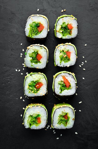 Sushi-Rolle mit Avocado-Gurke und Tomate Japanische Küche Draufsicht auf schwarzem Hintergrund