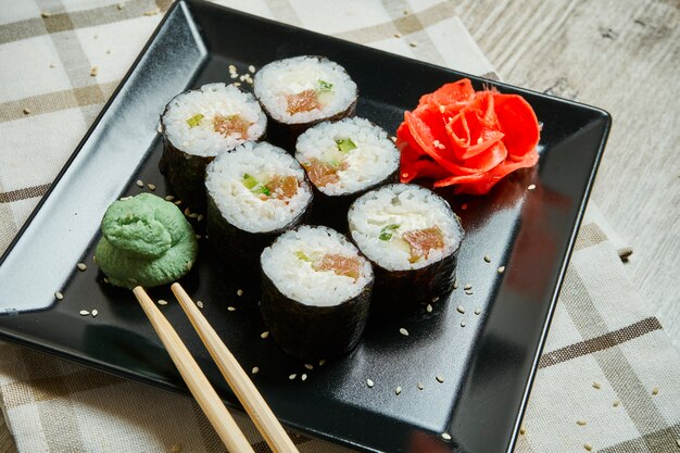 Sushi-Rolle mit Lachs auf einem schwarzen Teller auf einem Holztisch. Japanisches Essen. Meeresfrüchte