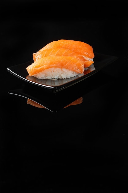 Sushi-Rolle mit Reflexion auf schwarzem Hintergrund. Ein Restaurant mit japanischer Küche. Frauenhände halten Sushi-Rollen