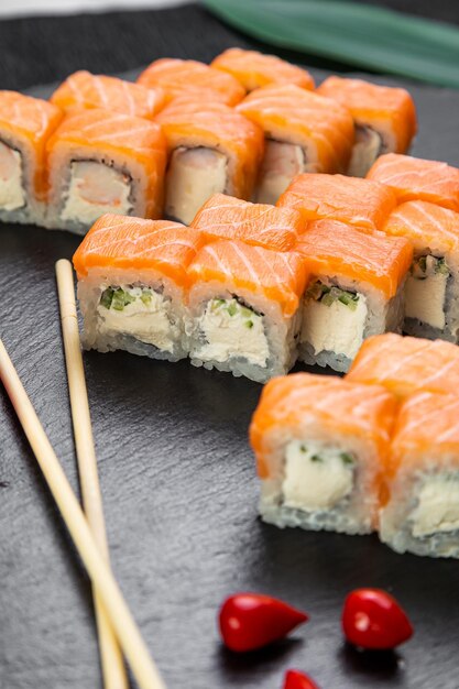 Sushi-Rollen auf dunklem Hintergrund, dekoriert mit Bambusblättern und Essstäbchen