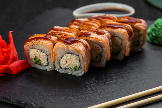 Sushi-Rollen auf dunklem Hintergrund, dekoriert mit Bambusblättern und Essstäbchen