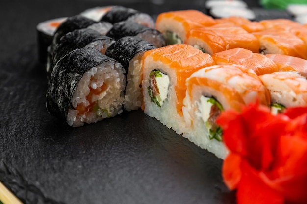 Sushi-Rollen auf dunklem Hintergrund, dekoriert mit Bambusblättern und Essstäbchen