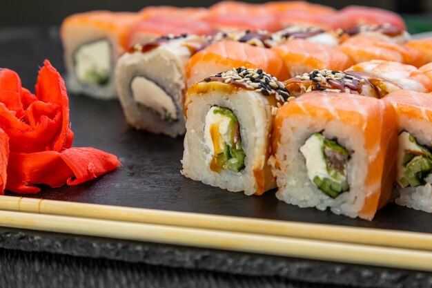 Sushi-Rollen auf dunklem Hintergrund, dekoriert mit Bambusblättern und Essstäbchen