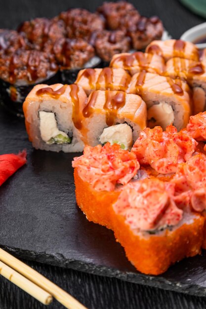 Sushi-Rollen auf dunklem Hintergrund, dekoriert mit Bambusblättern und Essstäbchen