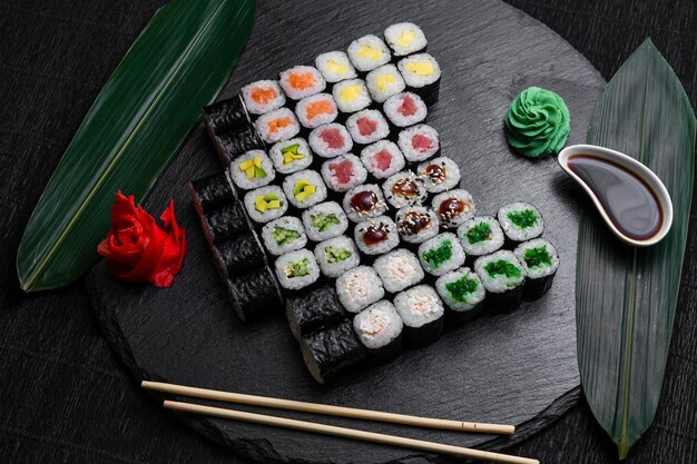 Sushi-Rollen auf dunklem Hintergrund, dekoriert mit Bambusblättern und Essstäbchen