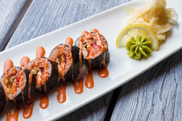 Sushi-Rollen auf weißem Teller. Wasabi und Zitrone neben Sushi. Bestes Gericht im Sushi-Café. Futomaki-Rollen serviert mit Gewürzen.