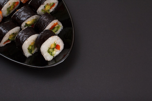 Sushi-Rollen in Nori-Algenblättern mit Avocado und rotem Fisch auf Keramikplatte. Draufsicht mit schwarzem Hintergrund und Kopienraum.