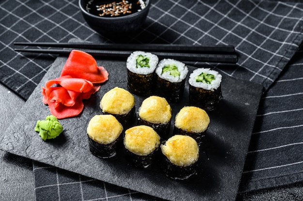 Sushi-Rollen mit Gurke, Lachs und Garnelen auf einem Steintablett. Schwarze Oberfläche. Draufsicht