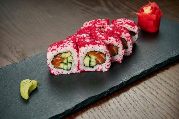 Sushi-Rollen mit Gurke, Tobico-Kaviar und Lachs auf einem schwarzen Schieferbrett auf einem Holztisch. Japanische Küche.