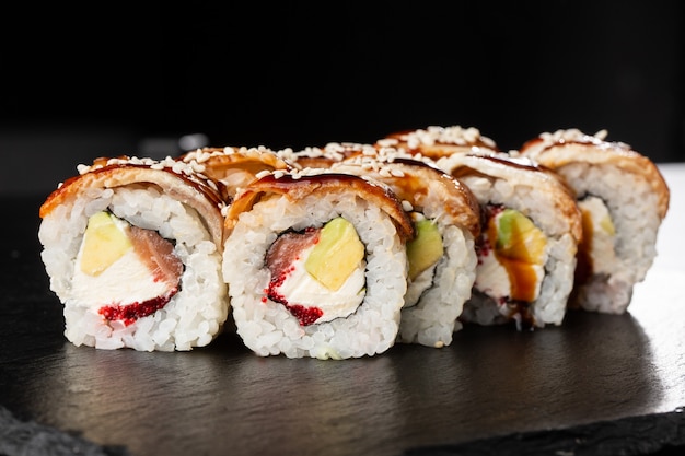 Sushi-Rollen mit Lachs, Avocado, Aal, fliegendem Fischkaviar und Frischkäse innen auf Schwarz