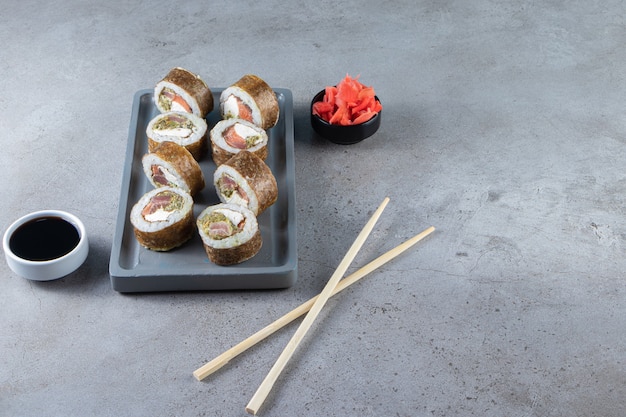 Sushi-Rollen, Sojasauce, Wasabi und eingelegter Ingwer auf Steinhintergrund.