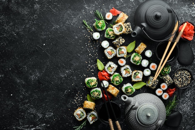 Sushi-rollen und teekanne mit tee auf schwarzem steinhintergrund tolles japanisches essen