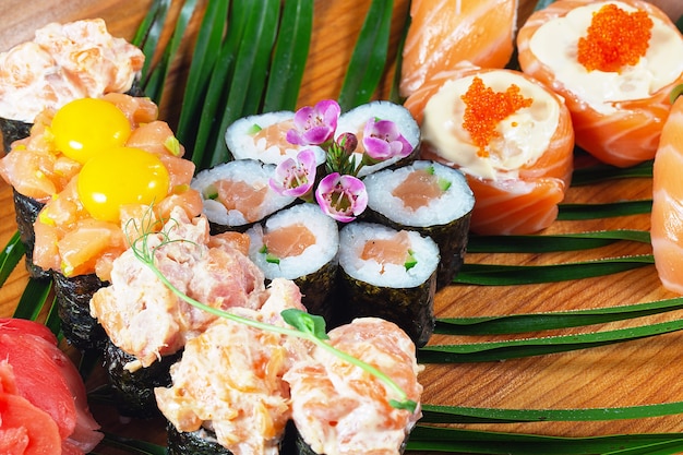 Sushi y rollos con salsa y huevos de codorniz crudos en una placa de madera con hojas verdes