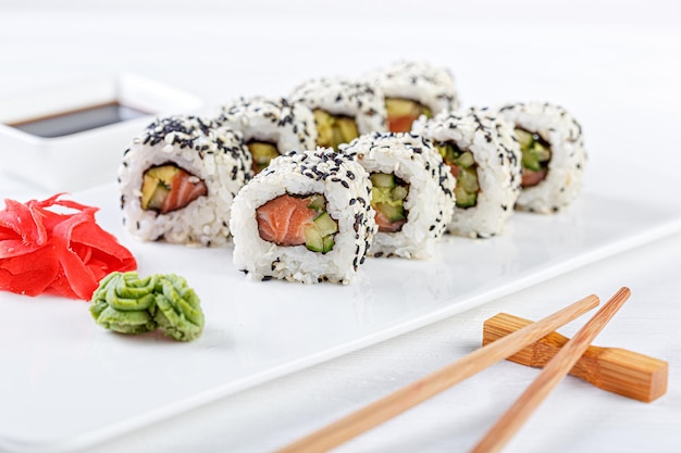 Sushi con salmón en un plato blanco con palillos de soja de jengibre wasabi sobre un fondo blanco