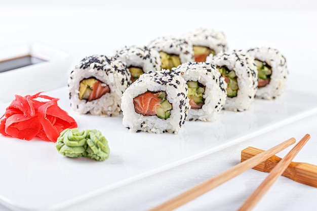 Sushi con salmón en un plato blanco con palillos de soja de jengibre wasabi sobre un fondo blanco