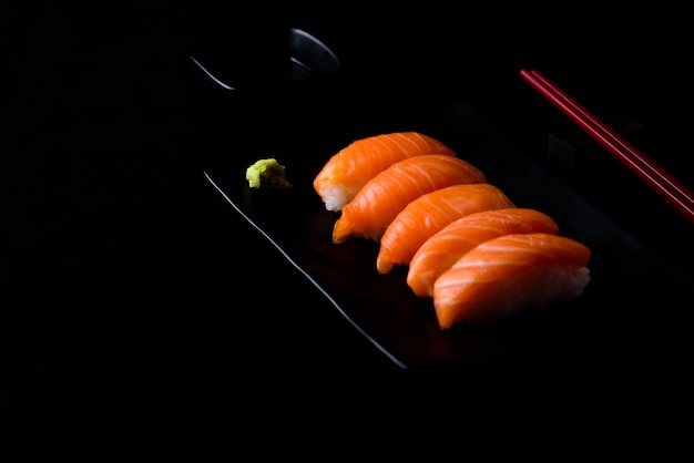 Sushi de salmón con wasabi verde en un plato o plato negro y salsa shoyu